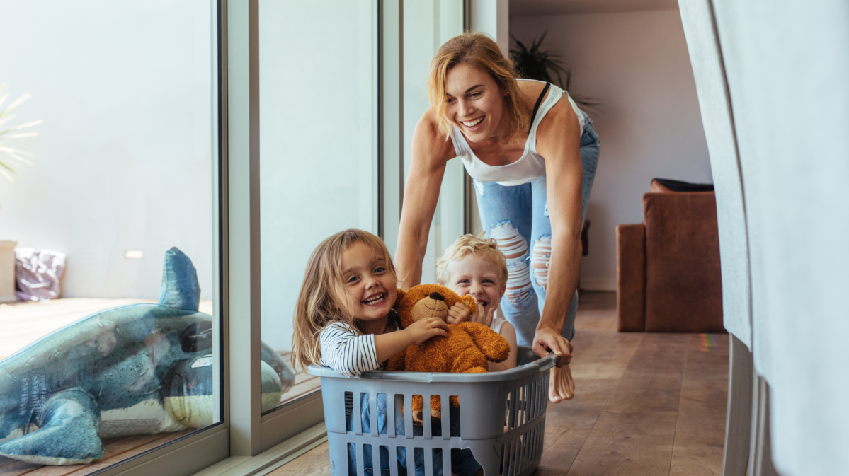 Eine Mutter schiebt ihren kleinen Sohn und ihre kleine Tochter in einem Wäschekorb durch die Wohnung