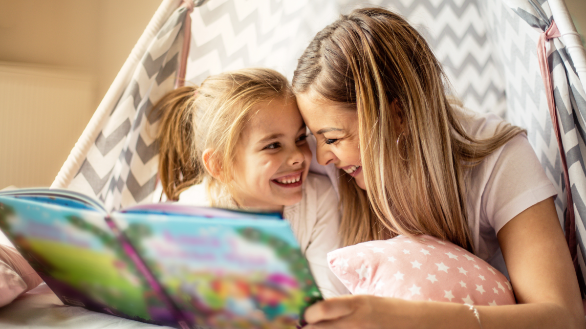 Mutter und Tochter liegen im Bett und schauen sich ein Buch an