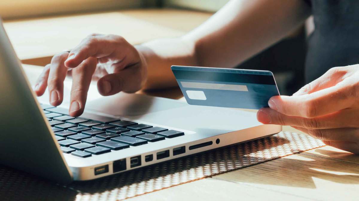 Frau tippt mit einer Hand auf dem Laptop und hält in der anderen Hand ihre Bankkarte.