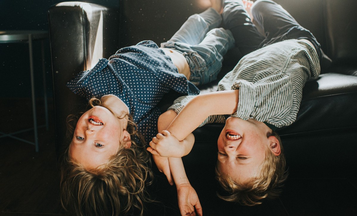 Zwei Kinder liegen Kopf nach unten auf einem dunklen Sofa