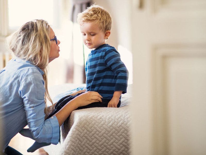 Mutter redet ernst mit ihrem Sohn, ca. 4 Jahre alt. Er sitzt auf dem Bett, sie hockt davor und redet auf Augenhöhe mit ihm.