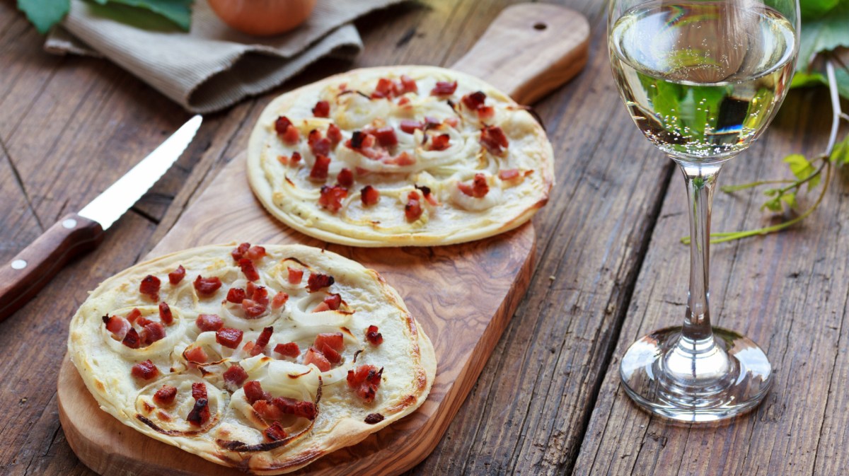 Zwei kleine runde Flammkuchen auf Holzbrett auf Tisch.