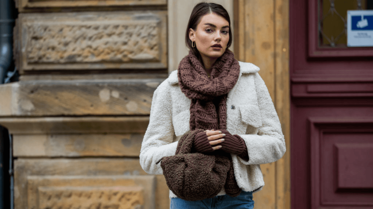 Celine Bethmann mit weißer Jacke und Teddy-Tasche vor Häuserwand.