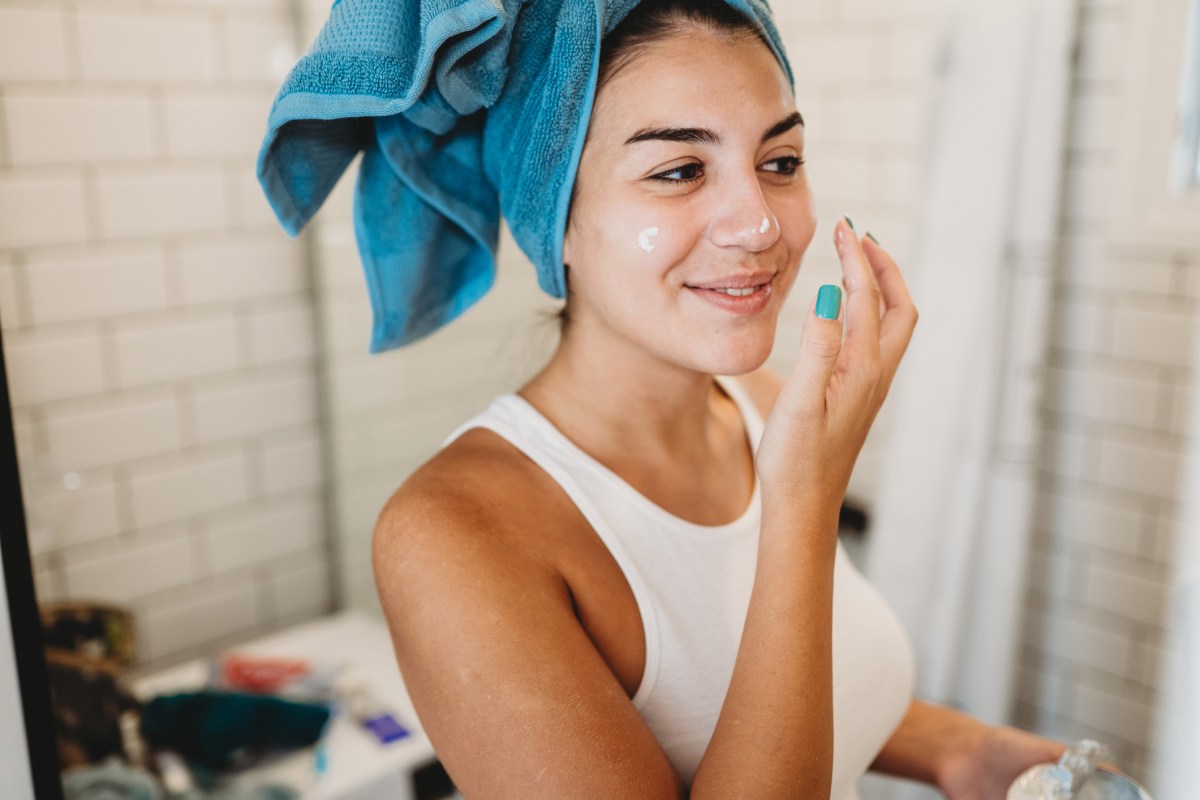 Frau mit Handtuchturban im Badezimmer trägt Creme auf Gesicht auf.