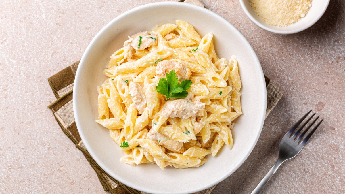 Penne mit Hähnchen und heller Soße auf einem weißen Teller.