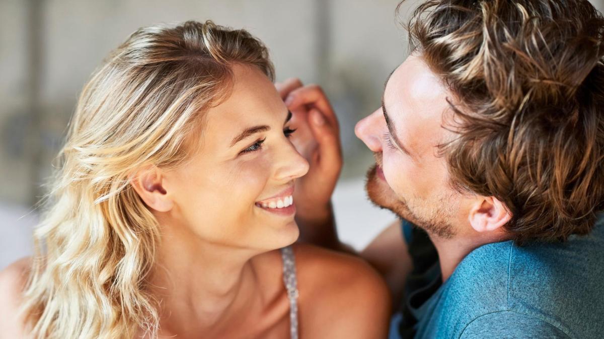 Ein lächelnder Mann streicht einer lächelnden Frau liebevoll die Haare aus dem Gesicht.