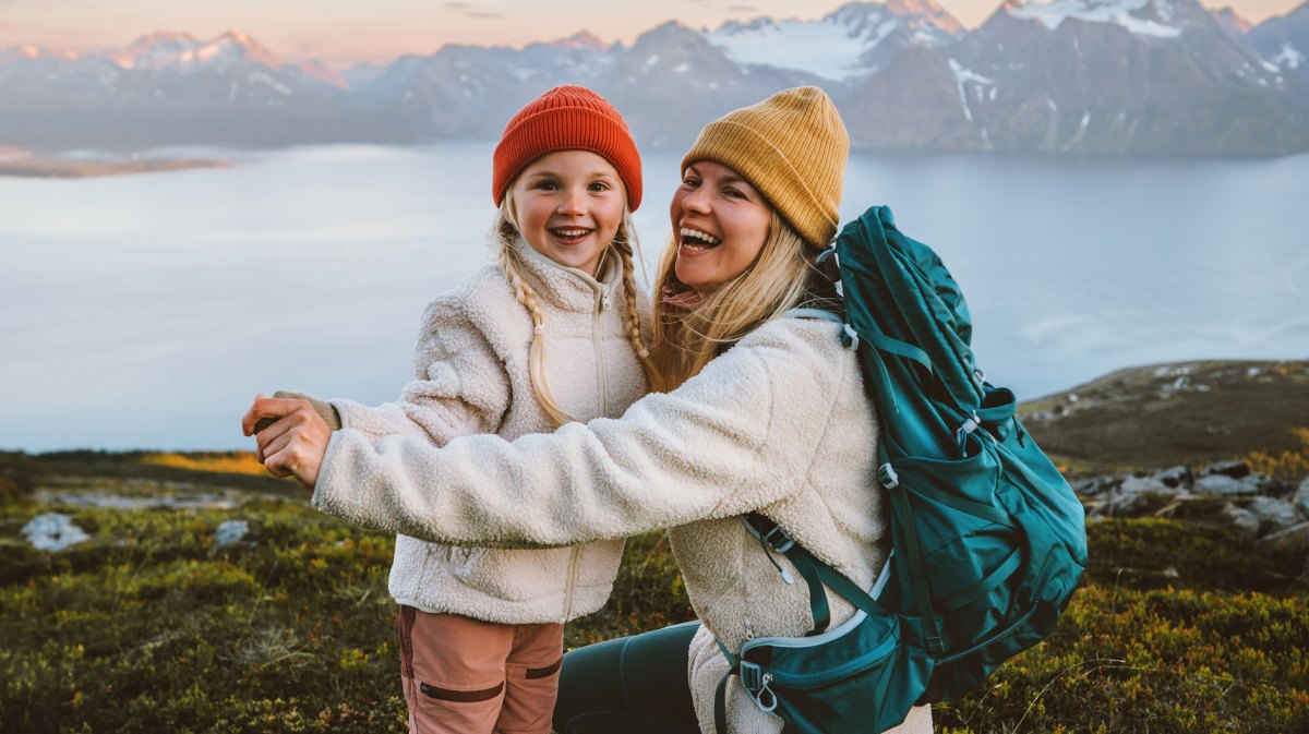 Mutter und Tochter in Outdoor Kleidung in einer bergigen Landschaft mit einem großen See im Hintergrund.