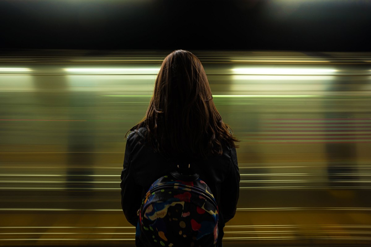 Frau steht am Bahngleis mit einem Rucksack