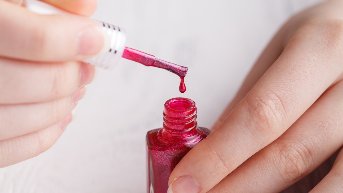 Frau hält Nagellack-Pinsel und Nagellack in der Hand.