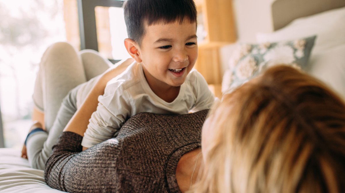 Mutter und Sohn liegen auf dem Boden. Der Sohn, ca. 4 Jahre alt, liegt auf dem Bauch seiner Mutter und lacht sie an.