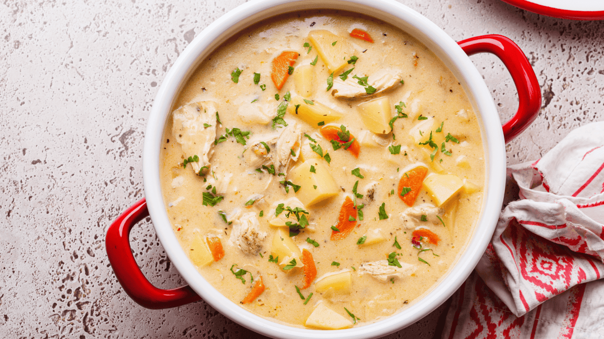 Hühnersuppe mit Sahne, Kartoffeln und Möhren in großem Topf.