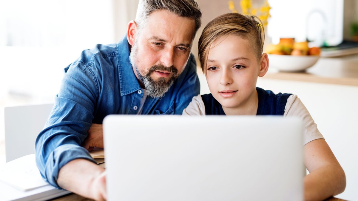 Vater und Sohn sitzen gemeinsam vorm Laptop und schauen sich etwas an.