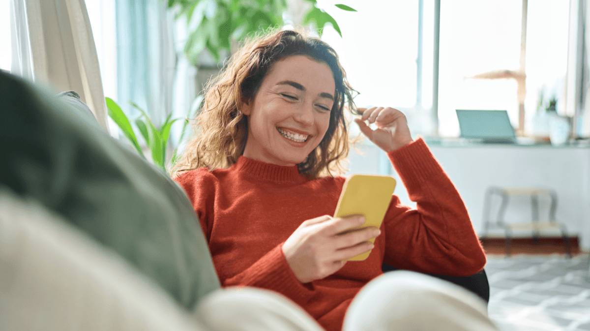 Junge Frau sitzt auf Sofa mit Handy in der Hand.