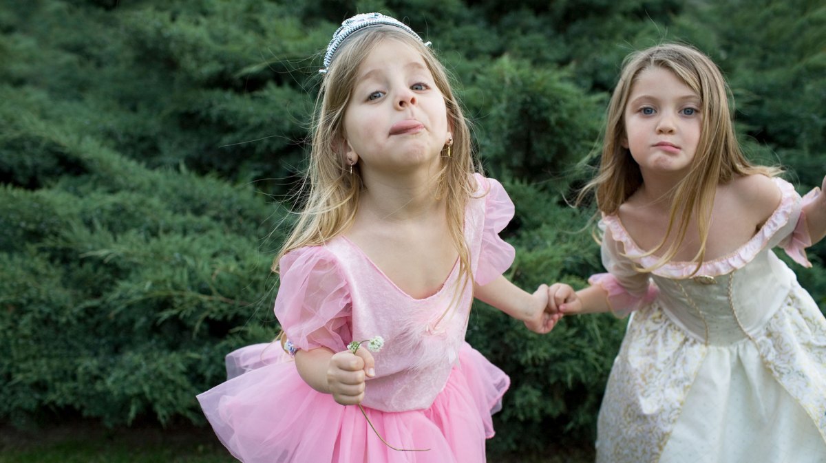 Zwei Mädchen, ca. 7 Jahre alt, stehen in Prinzessinnenkostümen im Garten und ziehen Grimassen Richtung Kamera.