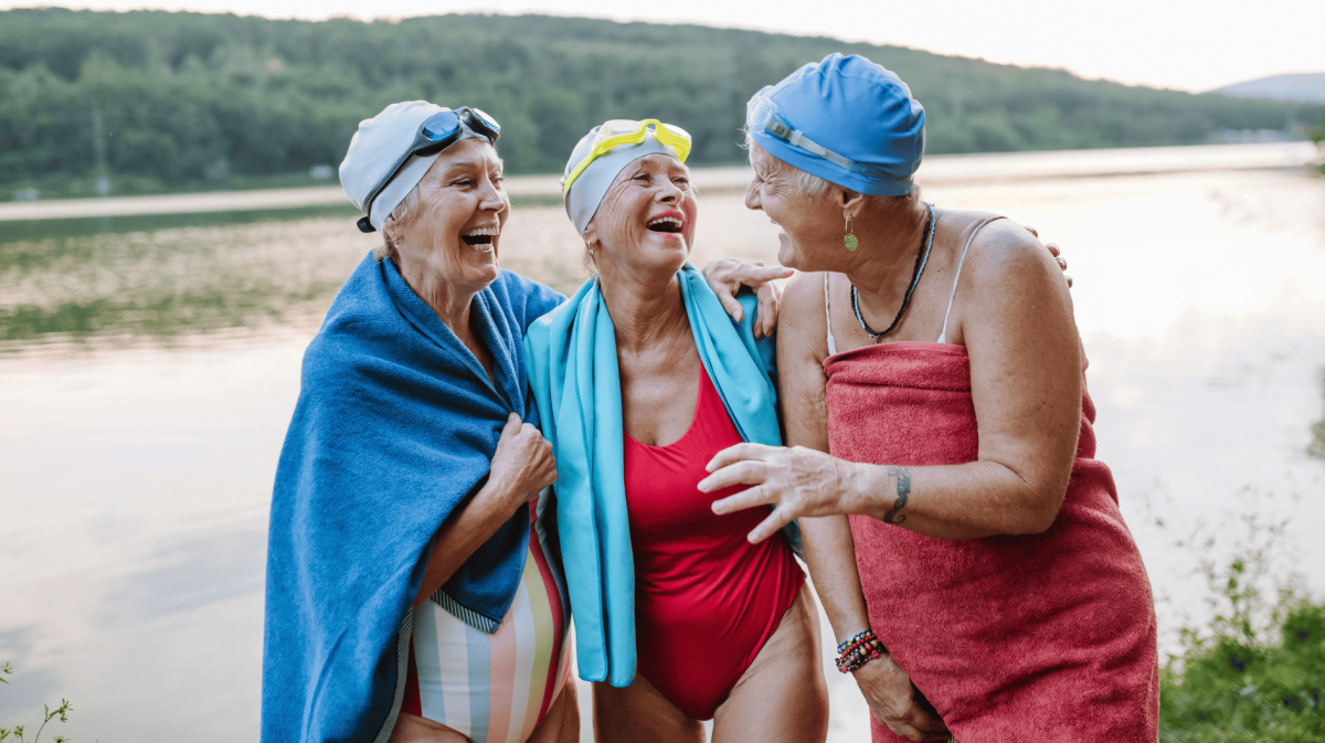 Drei ältere Frauen in Badekleidung vor einem See.